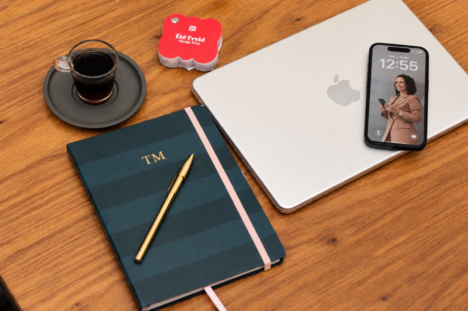 Mesa de trabalho com caderno TM, notebook, celular e café