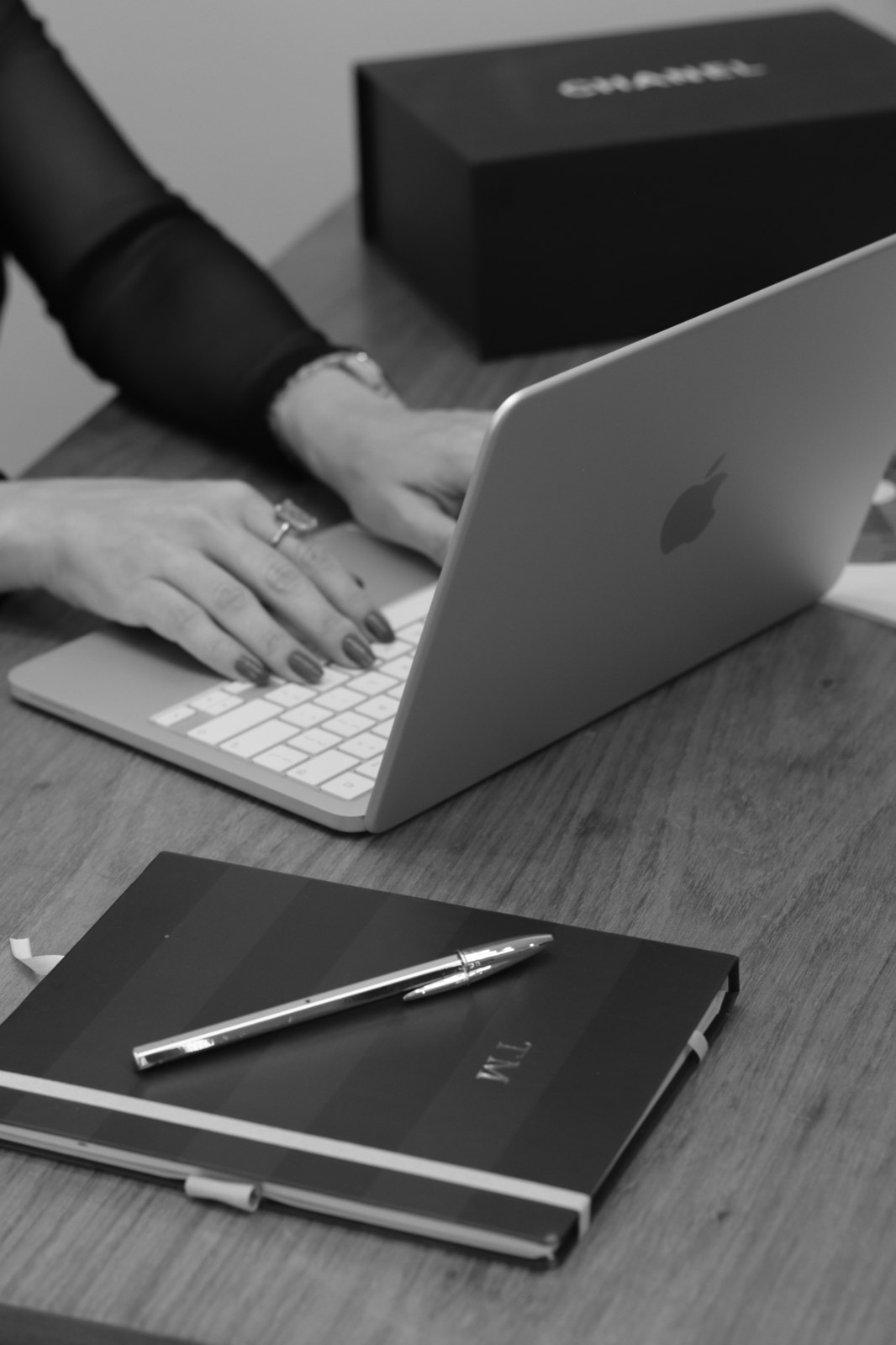 Mãos no notebook ao lado do caderno de anotações, em preto e branco