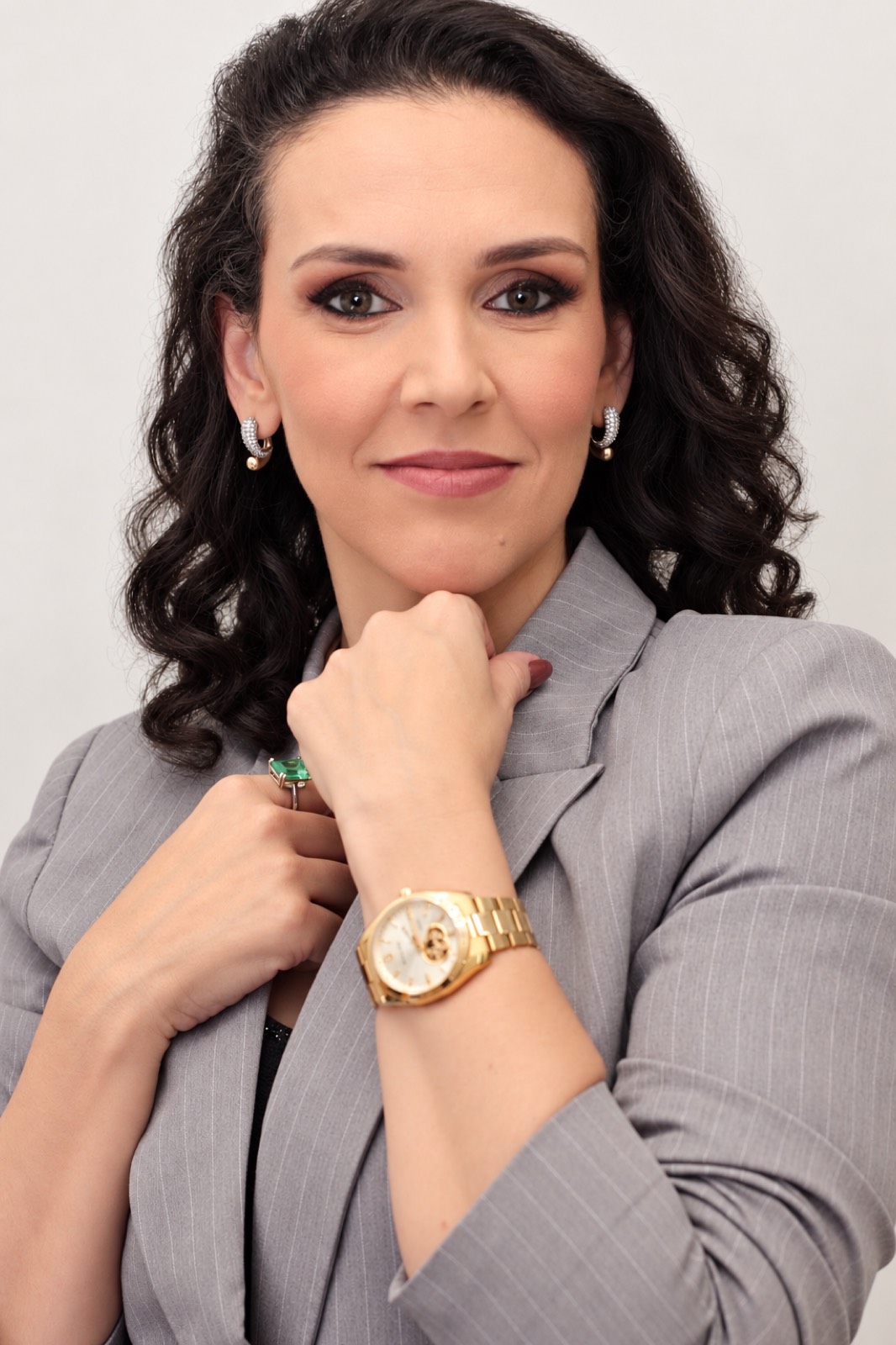 Tati Magalhães de blazer cinza, olhando para a câmera, com a mão apoiada no queixo